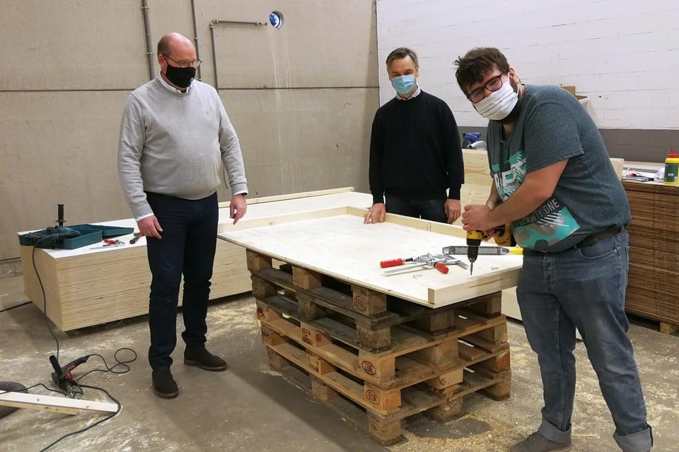 Dirk Mertens van Kaliber (links) en Luc Peetermans van De Bedstee (midden) kijken toe hoe medewerker Ragnan van maatwerkbedrijf Kaliber aan een houten onderdeel van Unieco werkt.