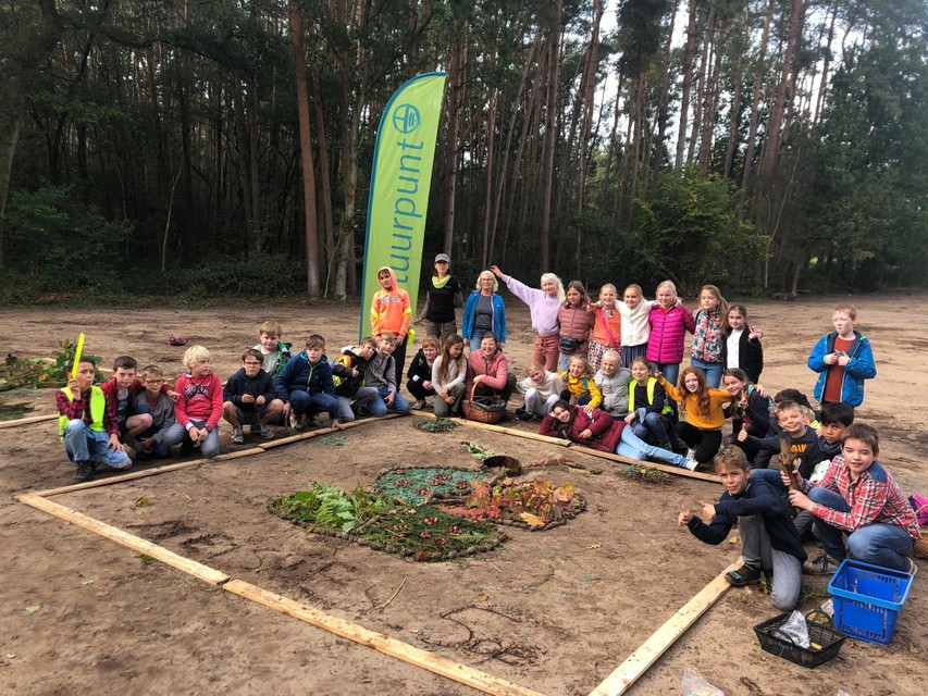 De leerlingen van het vijfde leerjaar van ‘t Klavernest staan bij het natuurschilderij dat de meisjes hebben gemaakt in de Visbeekvallei in Wechelderzande.