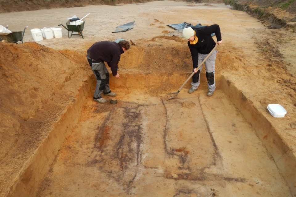 De lichamen en de kisten zijn vergaan, maar lieten in de grond een donkere verkleuring achter. De archeologen zijn hier bezig aan een dubbelgraf waarbij de kisten op houten dwarsbalken lagen.