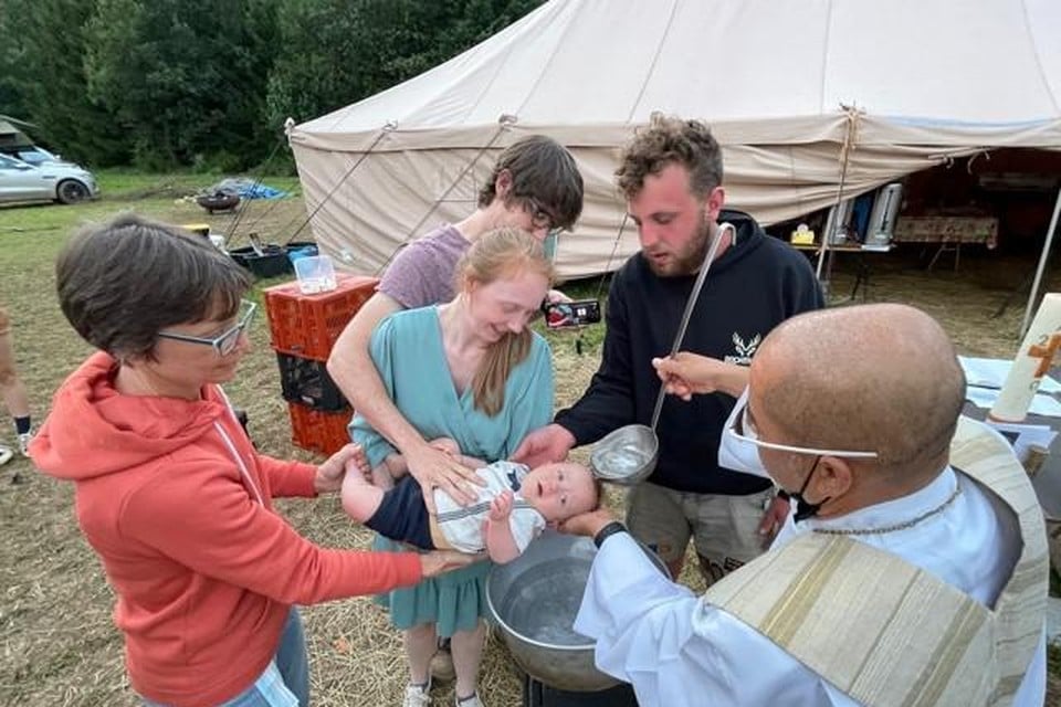 Pastoor Alvi doet met de pollepel het water over het hoofdje van Simon (of is het Lucas?) Ken en Bieke staan achter hun kindje.