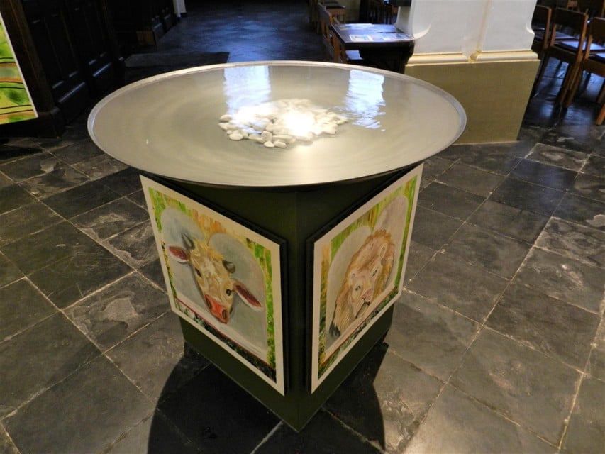 Op het voetstuk van de doopschaal met bewegend water staan de symbolen van de vier evangelisten. 