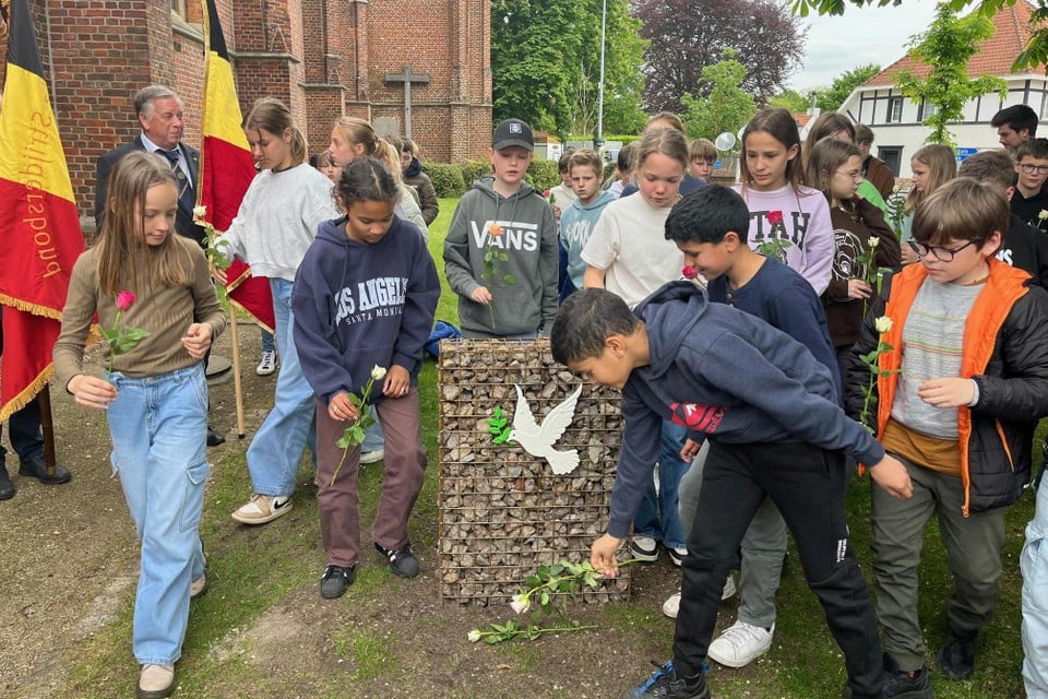 De zesdejaars van basisschool De Komeet in Gierle leggen rozen neer bij het gloednieuwe vredesmonument naast de kerk van het dorp.