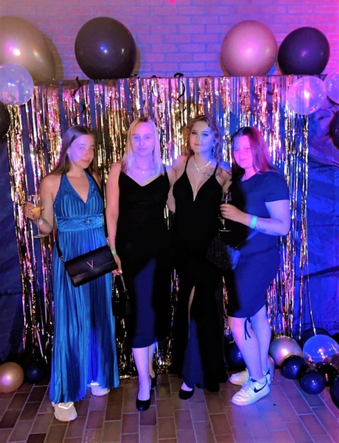 De drie organiserende dames en een medeleerlinge poseren in een passend decor met ballonnen en veel glitter. 