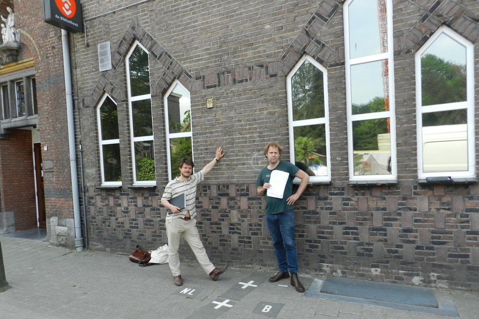 Paul Govaerts en Maarten Westra Hoekzema staan aan de grenslijn bij de ingang van het cultuurcentrum in Baarle.