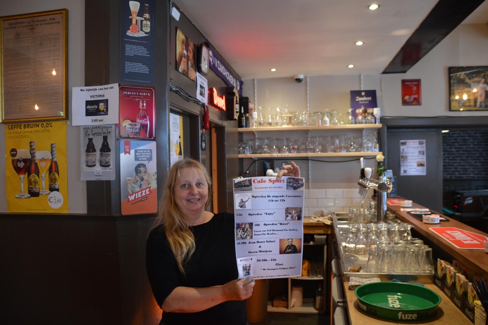 Sonja Tilleman van Café Sport met de affiche van wat zondag een hele dag livemuziek wordt op een podium naast het bekende volkscafé onder de kerktoren van Zandhoven.