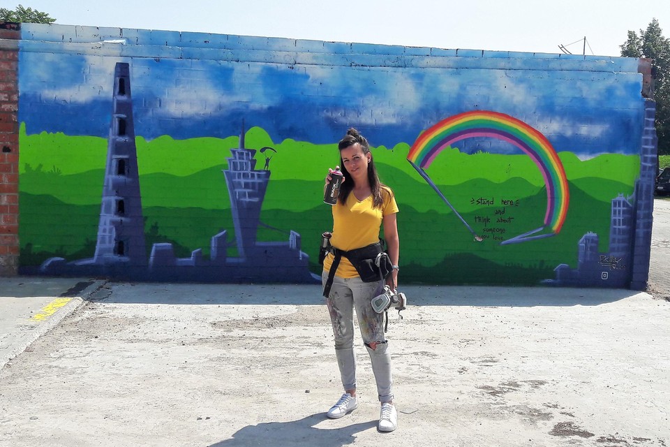 Isabelle Scheers, alias Bellie Ve, wil haar graffitikunsten op de wereld loslaten. Achter haar een van de twee realisaties aan de Kaai in Boom.
