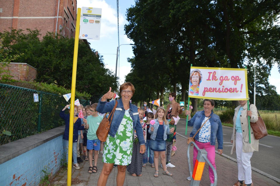 Juf Annemie net nadat ze uit de cabrio is gestapt aan de bushalte van Mariagaarde. Rechts enkele collega’s met spandoek.