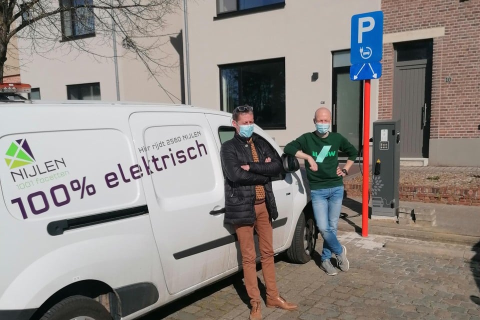 Schepenen Luc Luyten en Bert Celis met een elektrische auto van de gemeente bij de nieuwe laadpaal.