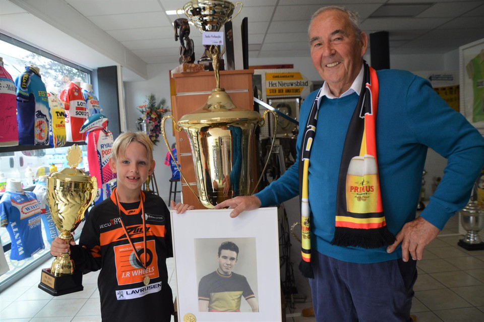 Jef Peeters (6) met zijn Belgische kampioensbeker en gouden medaille in het Kempens Wielermuseum naast opa Frans ‘Suske’ Verhaegen bij een portret van Frans als Belgisch kampioen bij de jeugd. De beker achter het portret won Frans in Valencia.