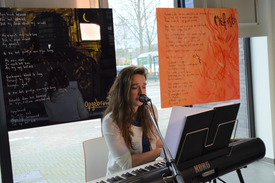 Helena Rymen aan de piano in de bibliotheek, met achter haar twee van de acht panelen waarop haar teksten staan.