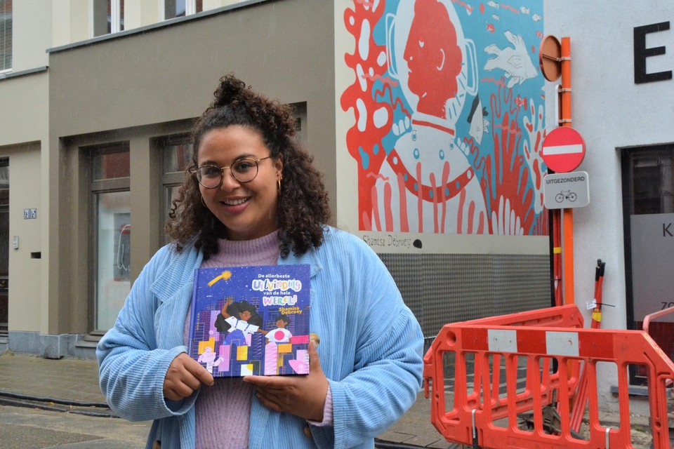 Shamisa Debroey met haar eerste kinderboek, aan haar muurschildering vlak bij de Adegemstraat in Mechelen.