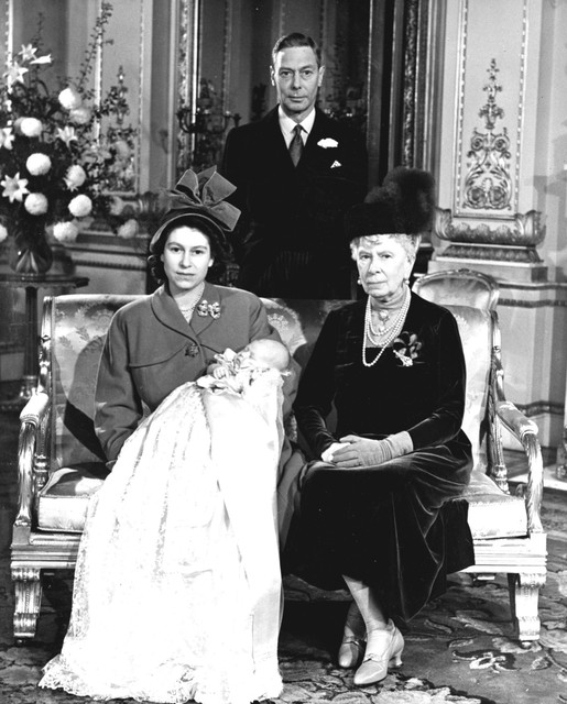 Princess Elizabeth met in haar handen Prince Charles, naast haar Queen Mary, de moeder van King George VI, die achter haar staat.  